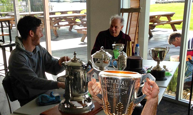 Members polishing trophies with AFL trophy.